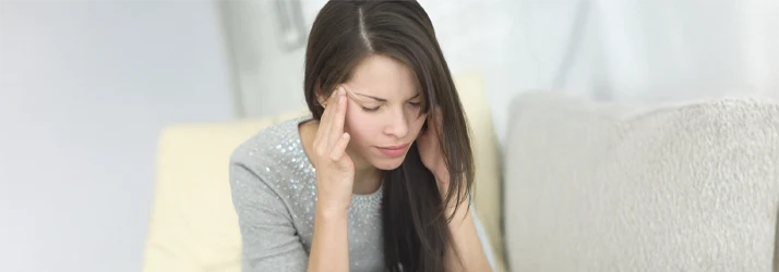 Person seated indoors with hands covering the sides of the head, suggesting a moment of physical discomfort or strain.