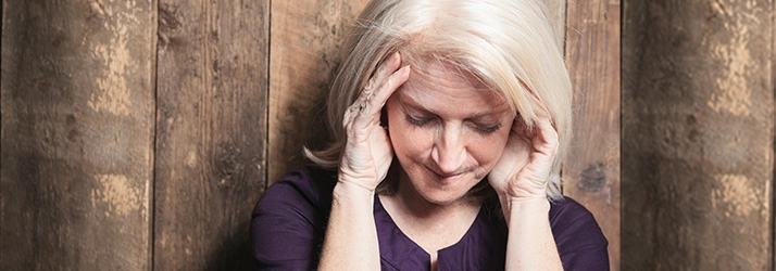 An individual with light-colored hair holding their head with both hands, suggesting tension or headache.