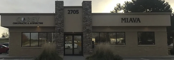 Exterior of the clinic building with signage reading “COREY Chiropractic & Acupuncture” and “MIAVA,” featuring stone accents and an entrance.