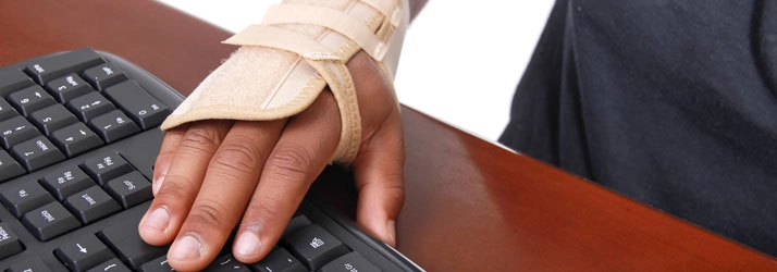 A hand wearing a wrist brace positioned on a computer keyboard.